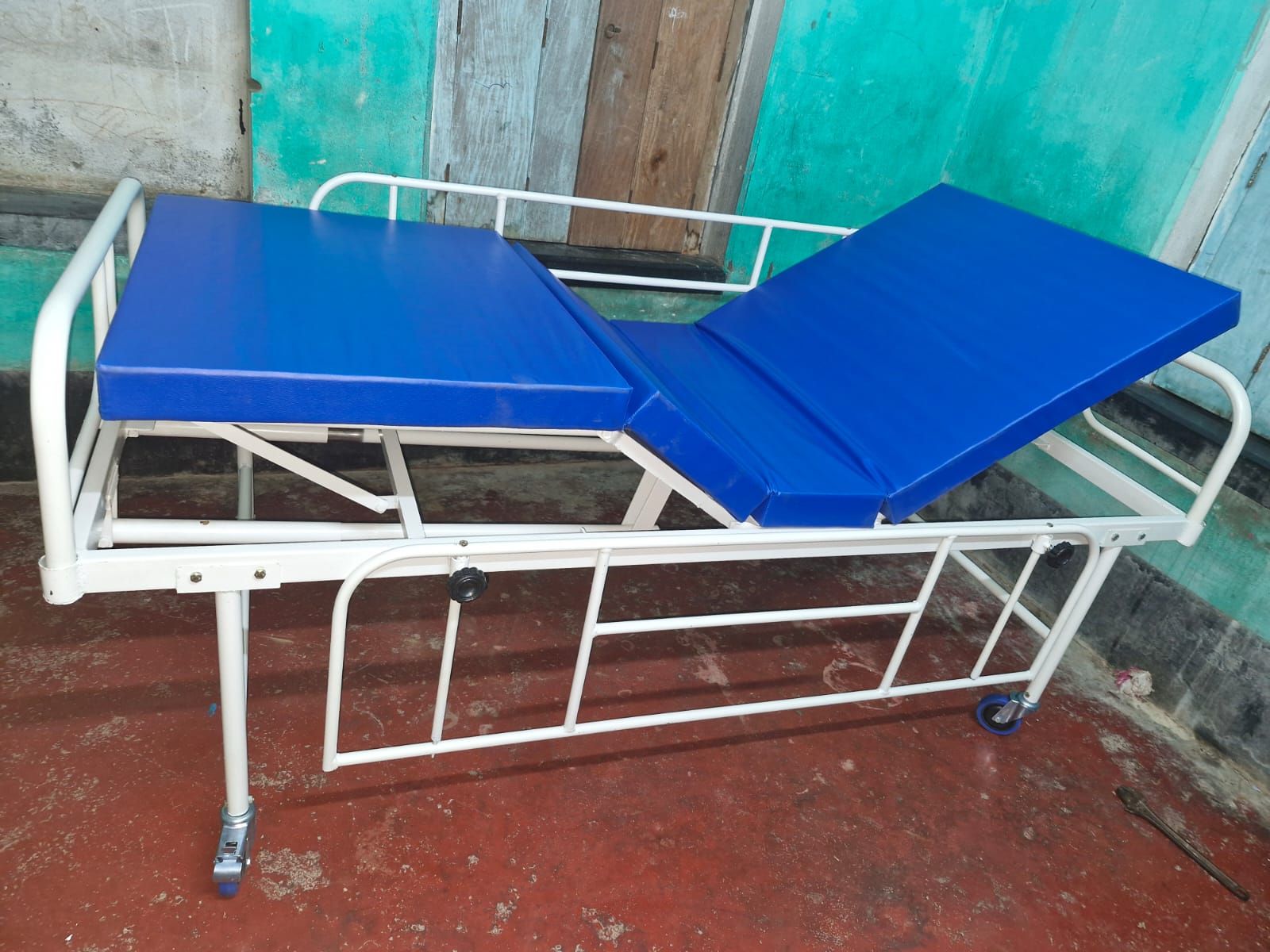 Blue Hospital Bed with metal frame against a green wall.